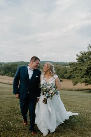 Newlyweds walk hand in hand across scenic hillside meadow with flowing wedding dress.