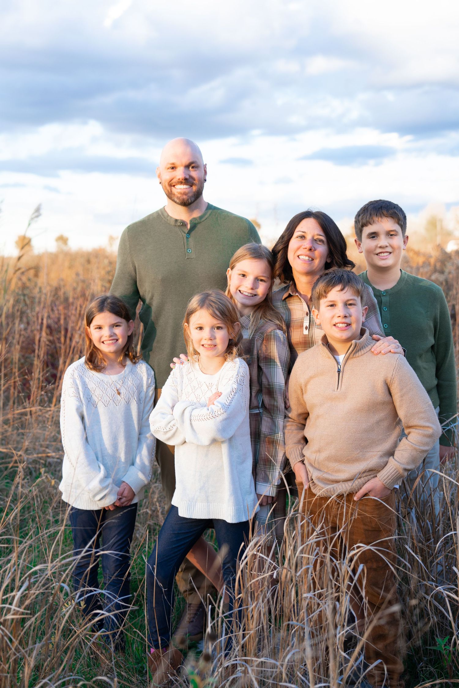 A happy family of four poses together by a waterfront with their newborn baby.