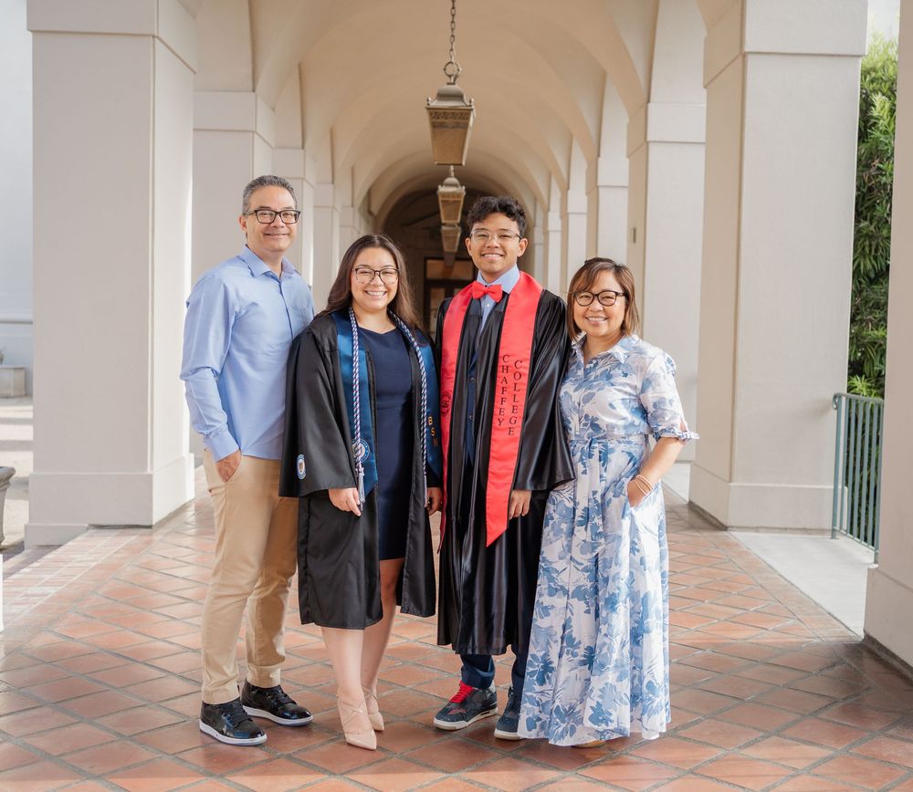 Family of four posing proudly with two graduates in robes under arched walkway.