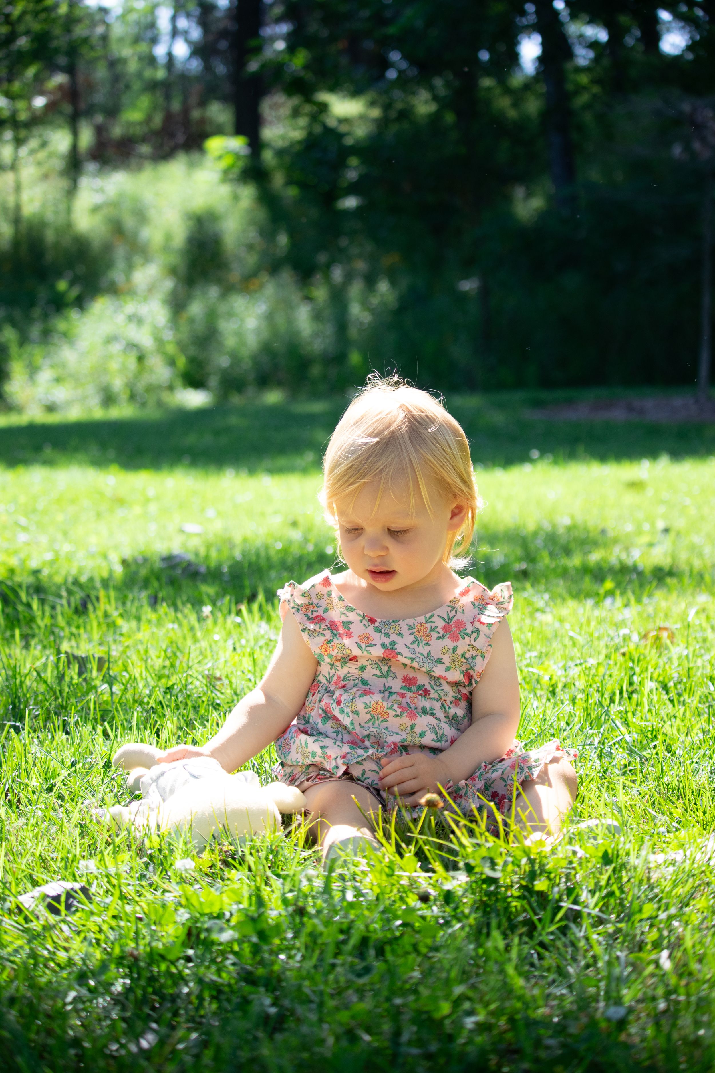 Small child sits on sunny grass wearing floral outfit on a warm summer day.