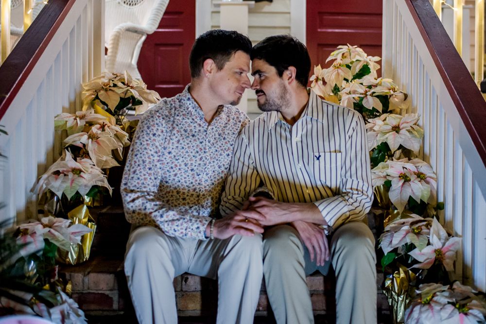 Two people sitting closely together on white stairs decorated with white and yellow floral arrangements.