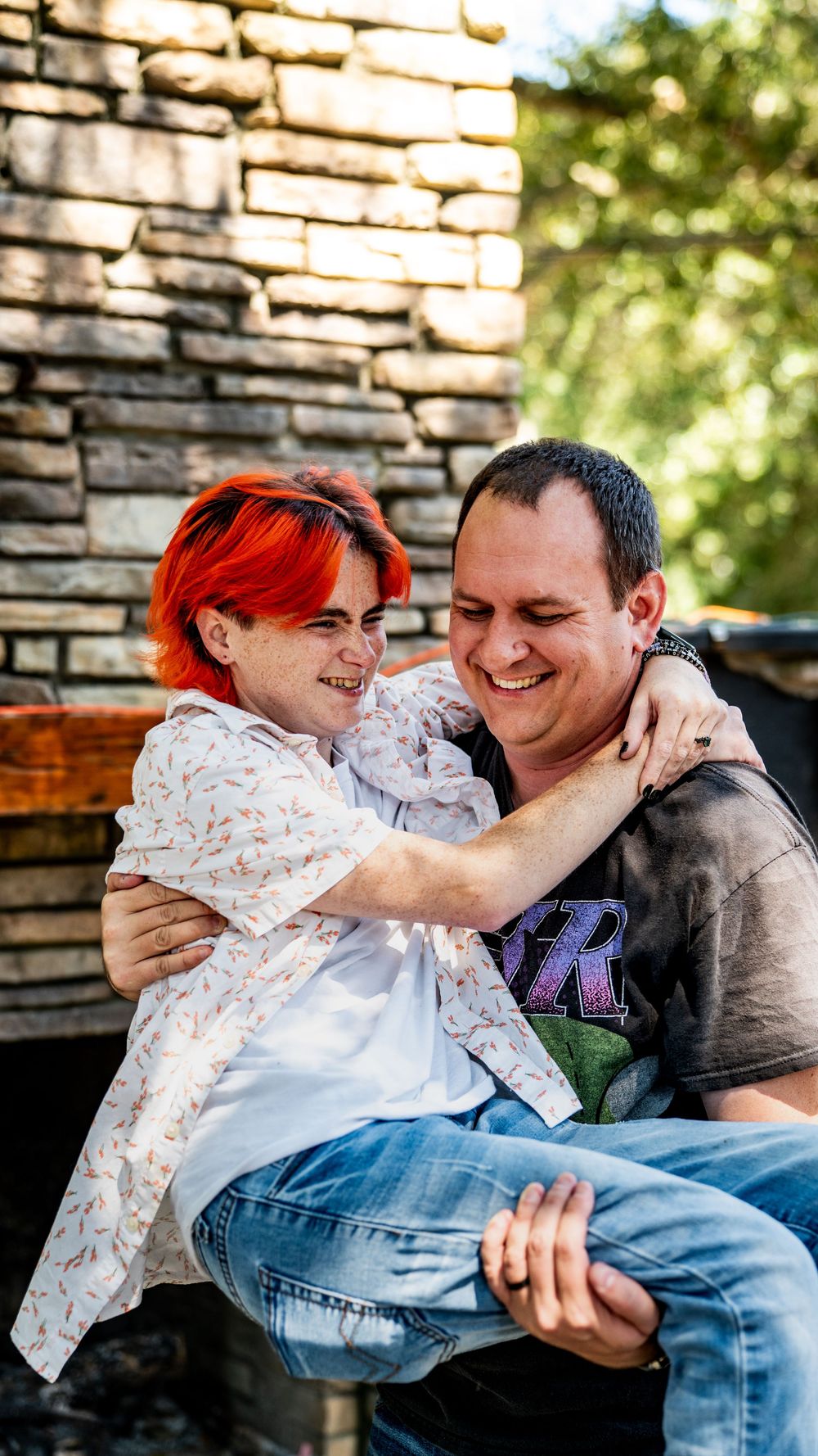 A playful couple shares intimate moments and laughter while sitting together against a brick wall outdoors.