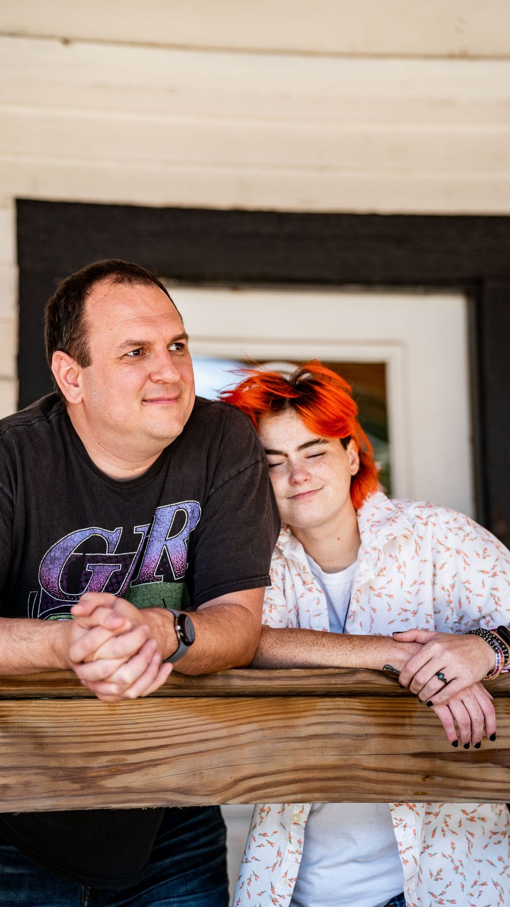 A couple leans together on a wooden railing in a casual indoor setting.