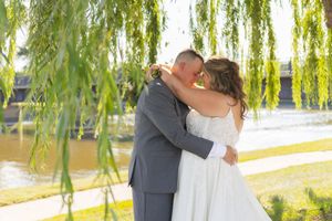 A couple embraces under beautiful willow tree branches during an outdoor summer wedding celebration.