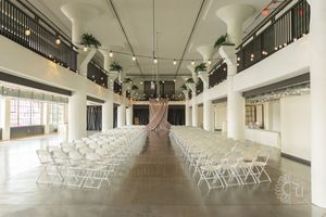 Panoramic view of an indoor wedding venue with white chairs arranged in rows and modern interior lighting.