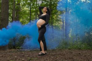 A person stands in a misty forest surrounded by blue smoke creating an ethereal atmosphere during a photo shoot.