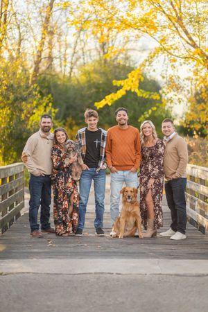A group poses together on a wooden bridge during golden hour with autumn foliage in the background.