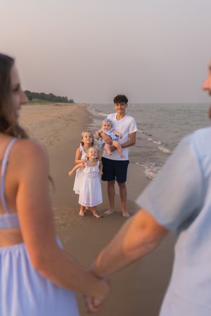 Family gathering at sunset on a peaceful beach with people in white and blue outfits standing along the shoreline.