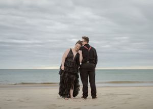 Couple embracing on sandy beach under cloudy sky.