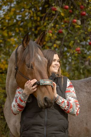 Brown horse and person share tender moment in front of autumn apple tree.