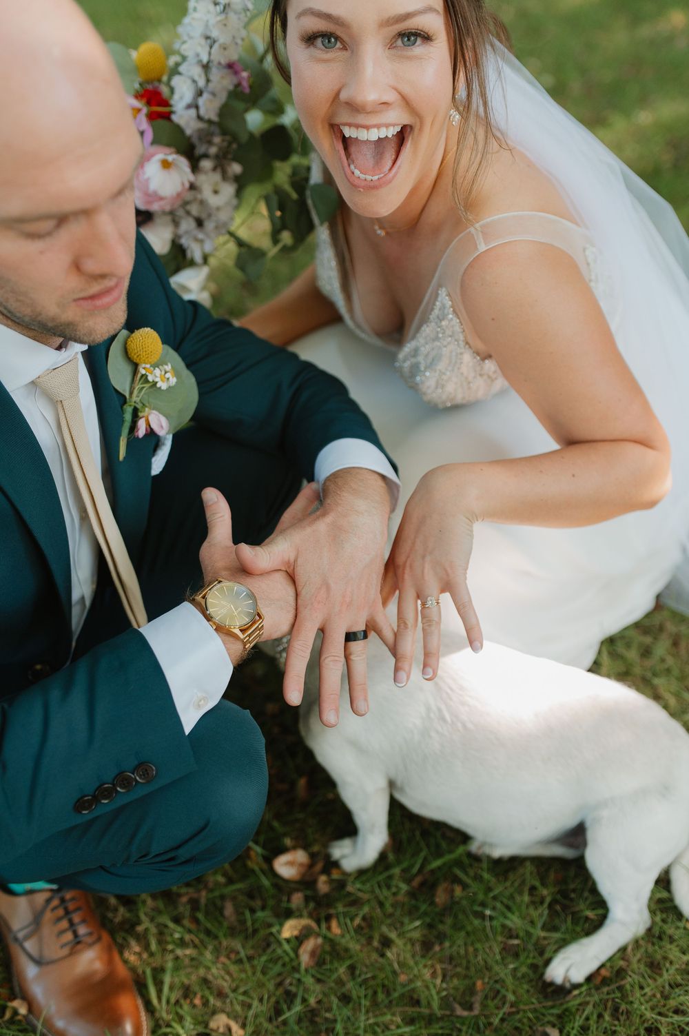 Wedding couple showing off rings with playful expressions outdoors.