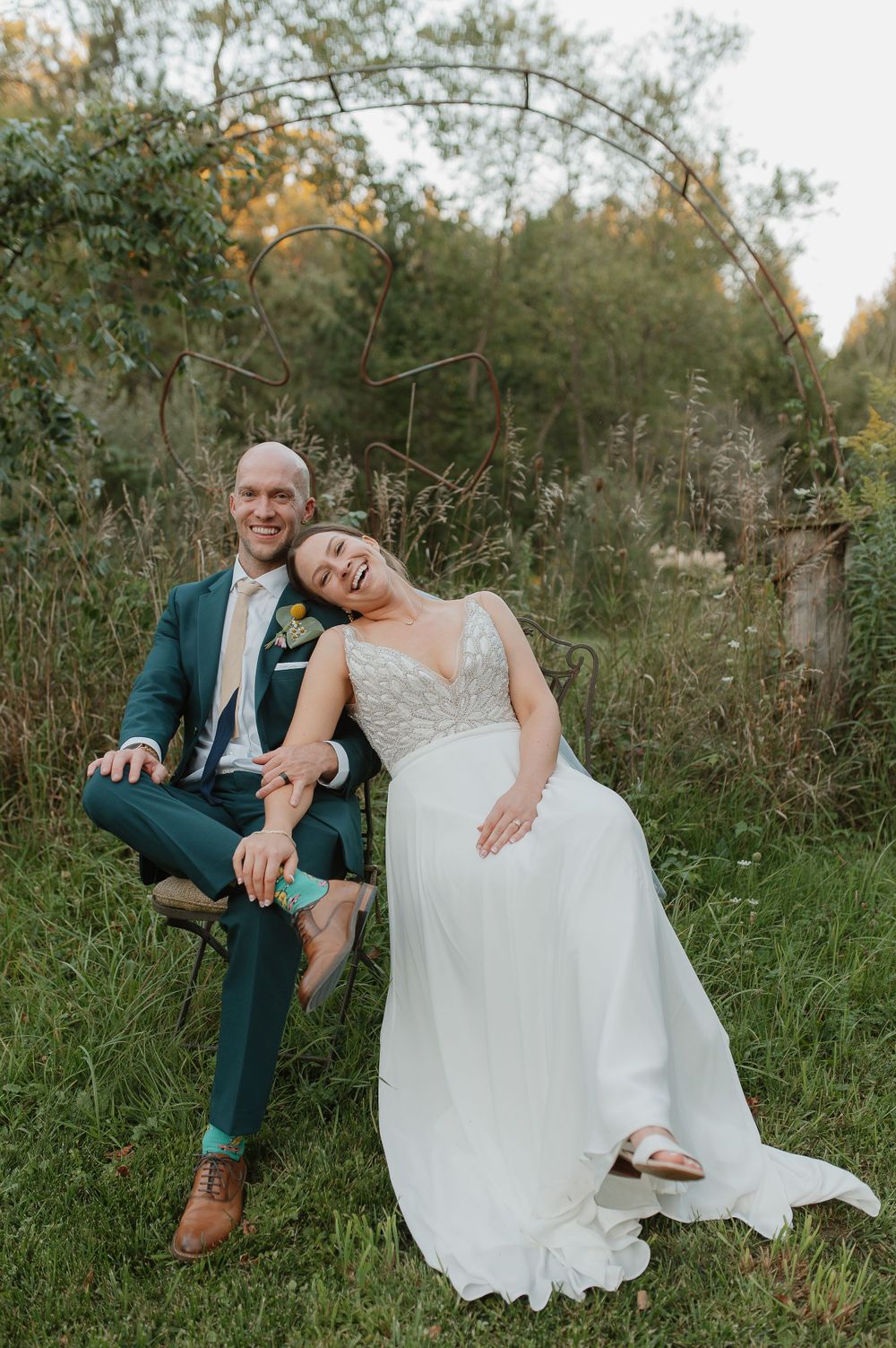 Romantic wedding portrait of couple relaxing on bench under metal garden arch.