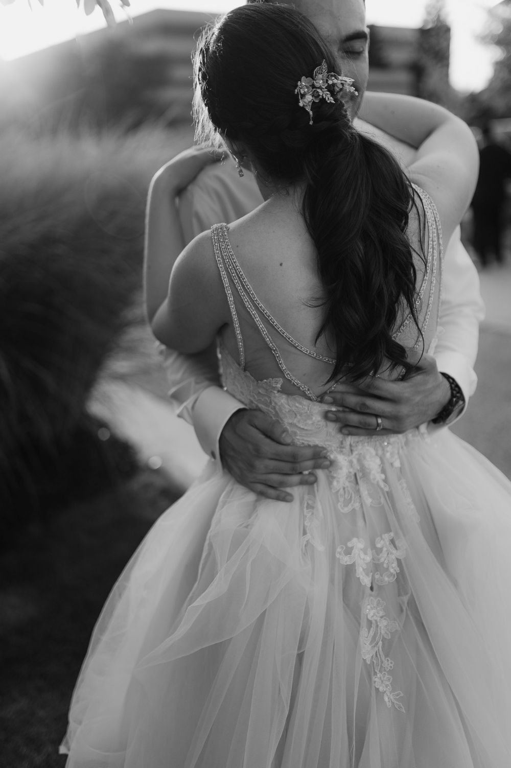Black and white photo showcasing intricate beaded back detail of wedding dress during embrace.