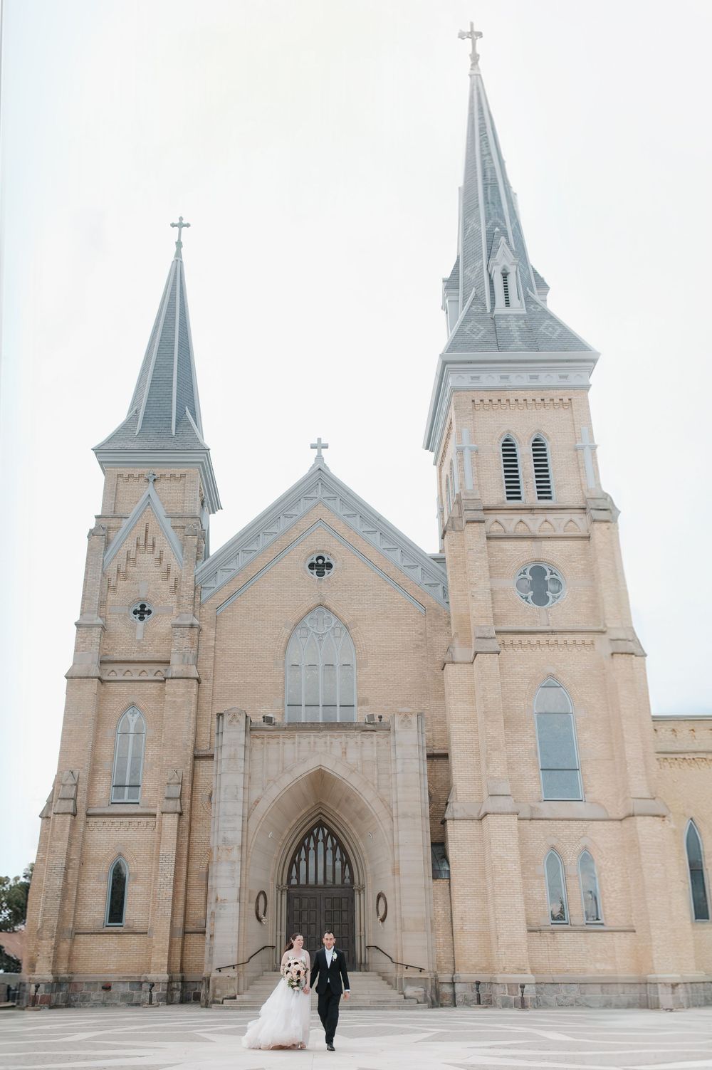 Traditional church exterior with twin spires serves as backdrop for wedding photograph.