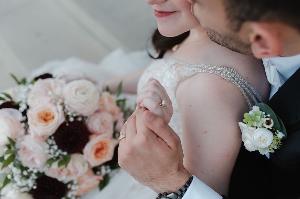 Close up wedding photo showing peach roses and white floral bouquet with a delicate lace dress detail.