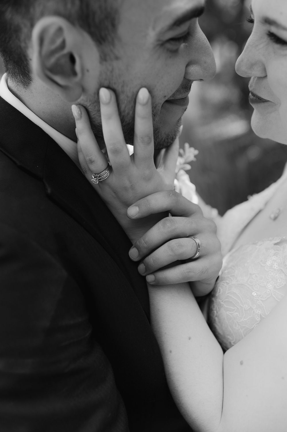 Black and white intimate wedding portrait showing hands with wedding rings in tender embrace.