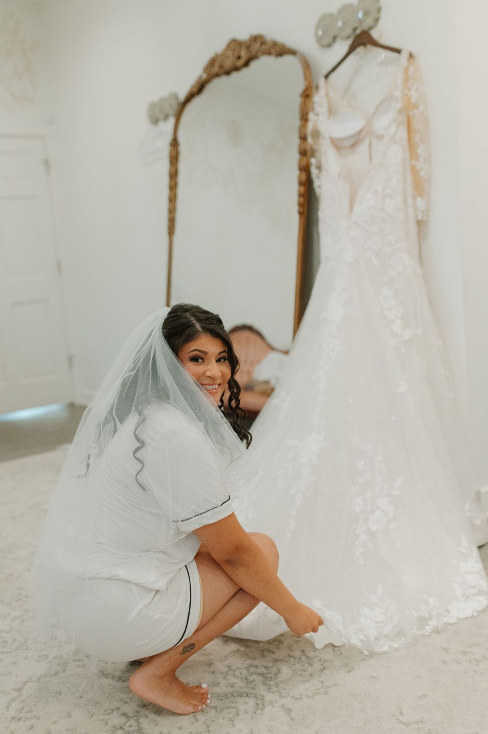 Wedding dress hanging on mirror with person in bridal robe.