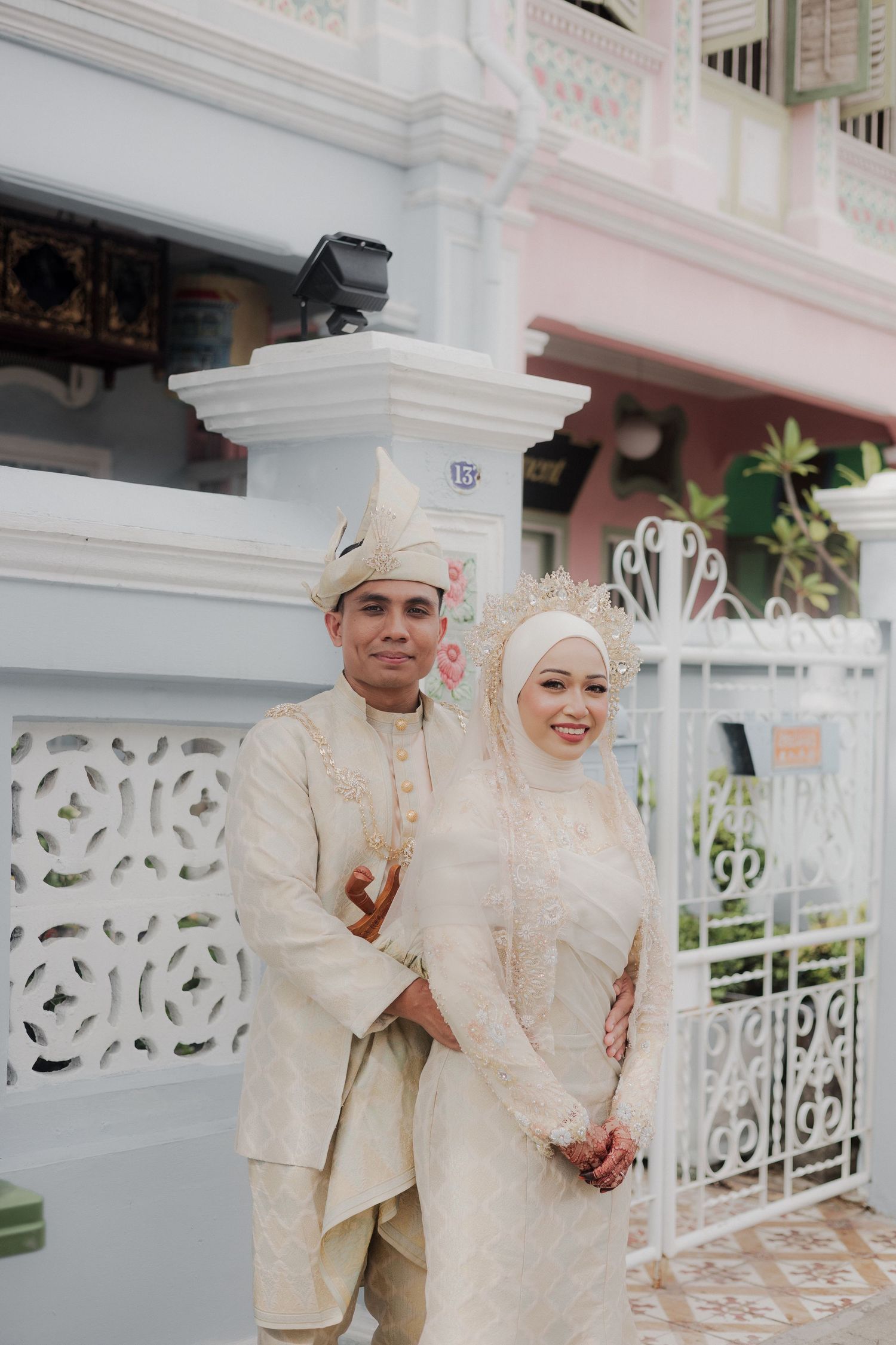 Traditional bridal portrait in emerald green dress with gold embroidery and white bouquet on urban street.