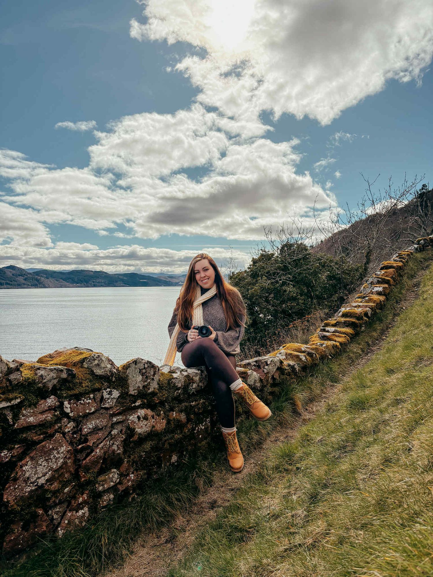 Woman in white sweater and blue jeans walking outdoors in Scotland setting with trees in background