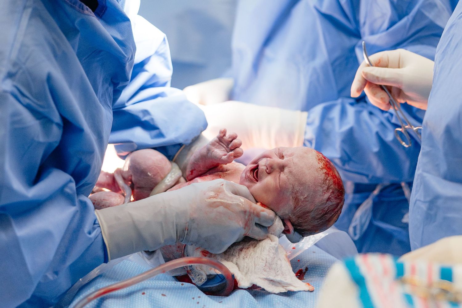 Medical professional performs surgery in dimly lit operating room with blue draping.