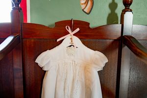 A row of vintage white lace christening gowns displayed on wooden hangers against a wall.