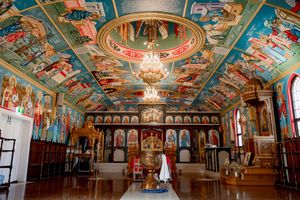 Ornate Orthodox church interior with colorful ceiling frescoes, chandeliers, and traditional iconography spanning the walls.
