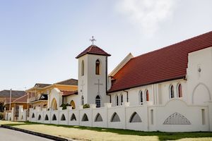 Panoramic exterior view of white church buildings with red roofs arranged in a row against a clear sky.