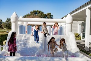 Children playing in a white inflatable bounce house with colorful decorations at an outdoor party.
