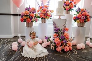 Pink balloon and floral party decorations with coral and purple flowers arranged against a white backdrop.