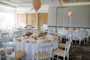 White-themed wedding reception setup with round tables, chiavari chairs, and soft natural lighting in modern venue.
