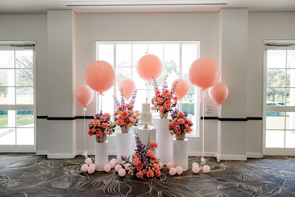 Modern event space with pink balloons and floral arrangements decorating a bright white room with large windows.