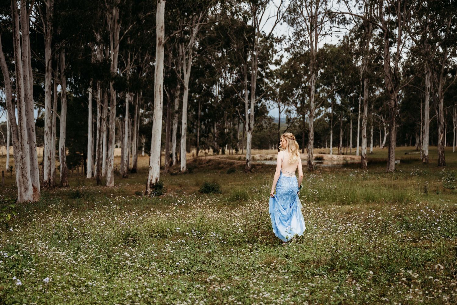 A figure in a flowing coral dress stands in golden sunlit grassland.