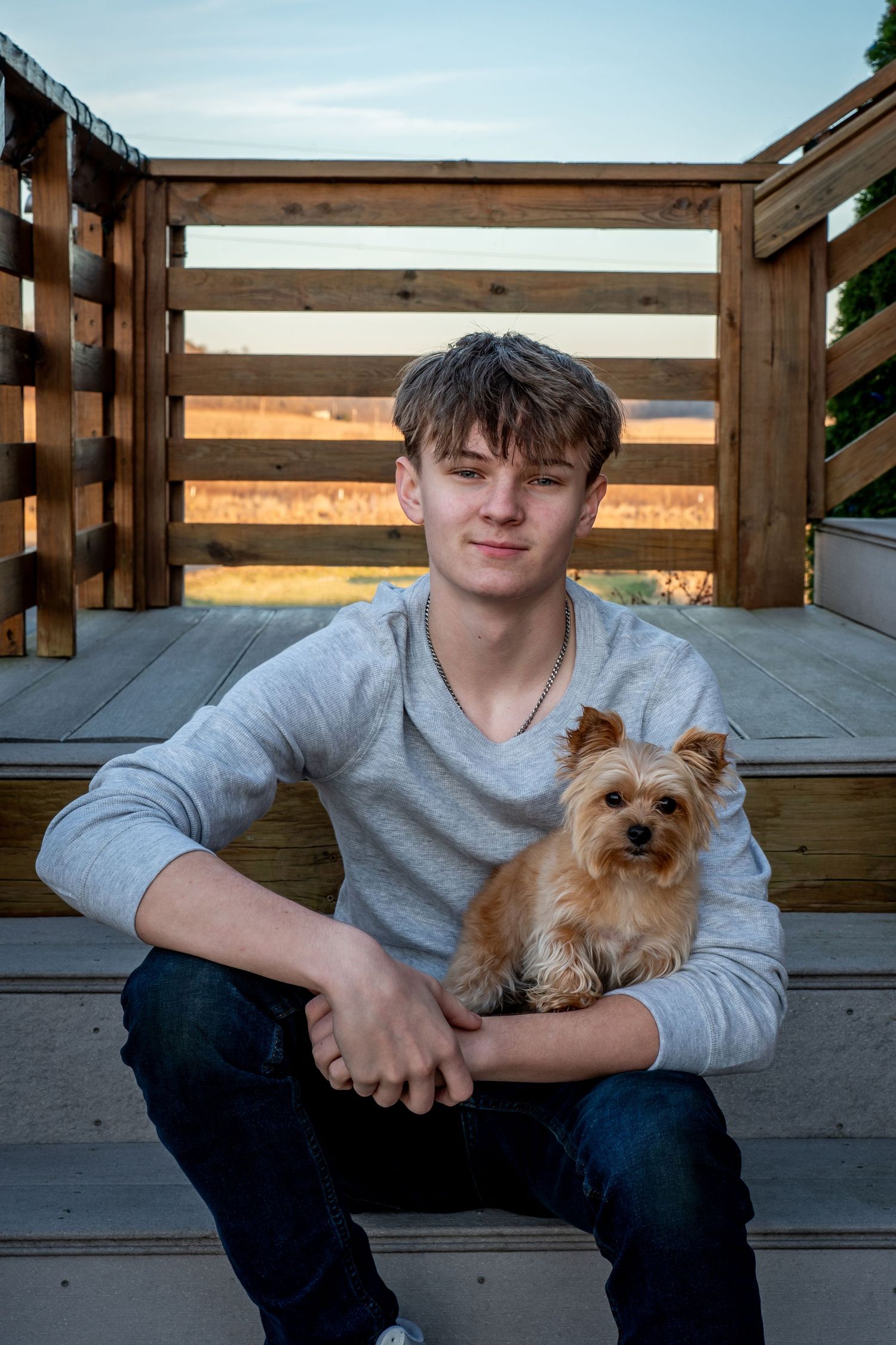 A Yorkshire Terrier puppy sits on wooden deck steps with their companion in front of a slatted wood backdrop.