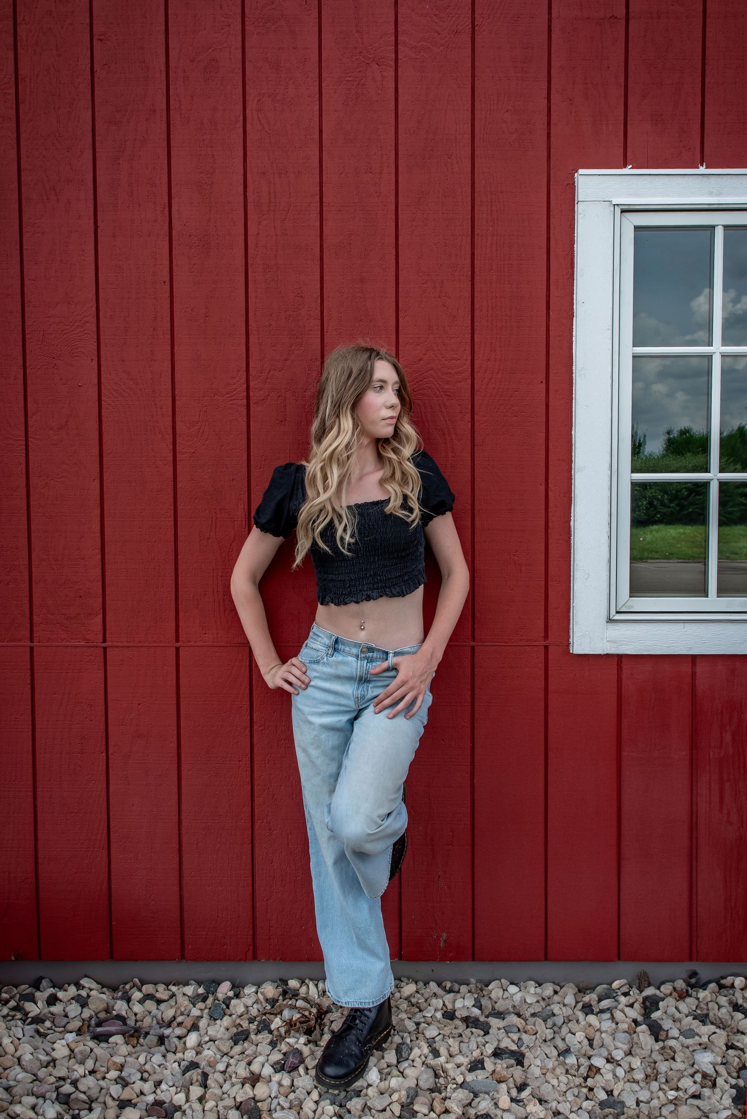 Fashion portrait against red barn wall featuring casual crop top and baggy jeans style with black boots.