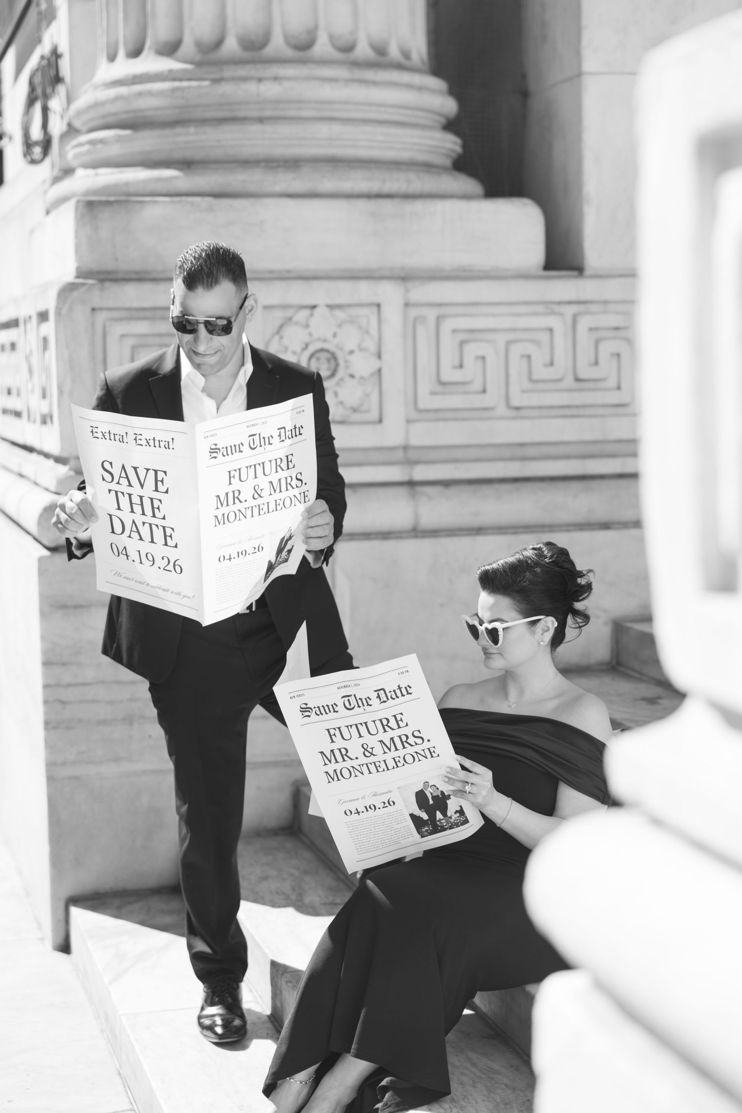 Couple holding Save the Date newspapers on steps in black and white engagement photo.