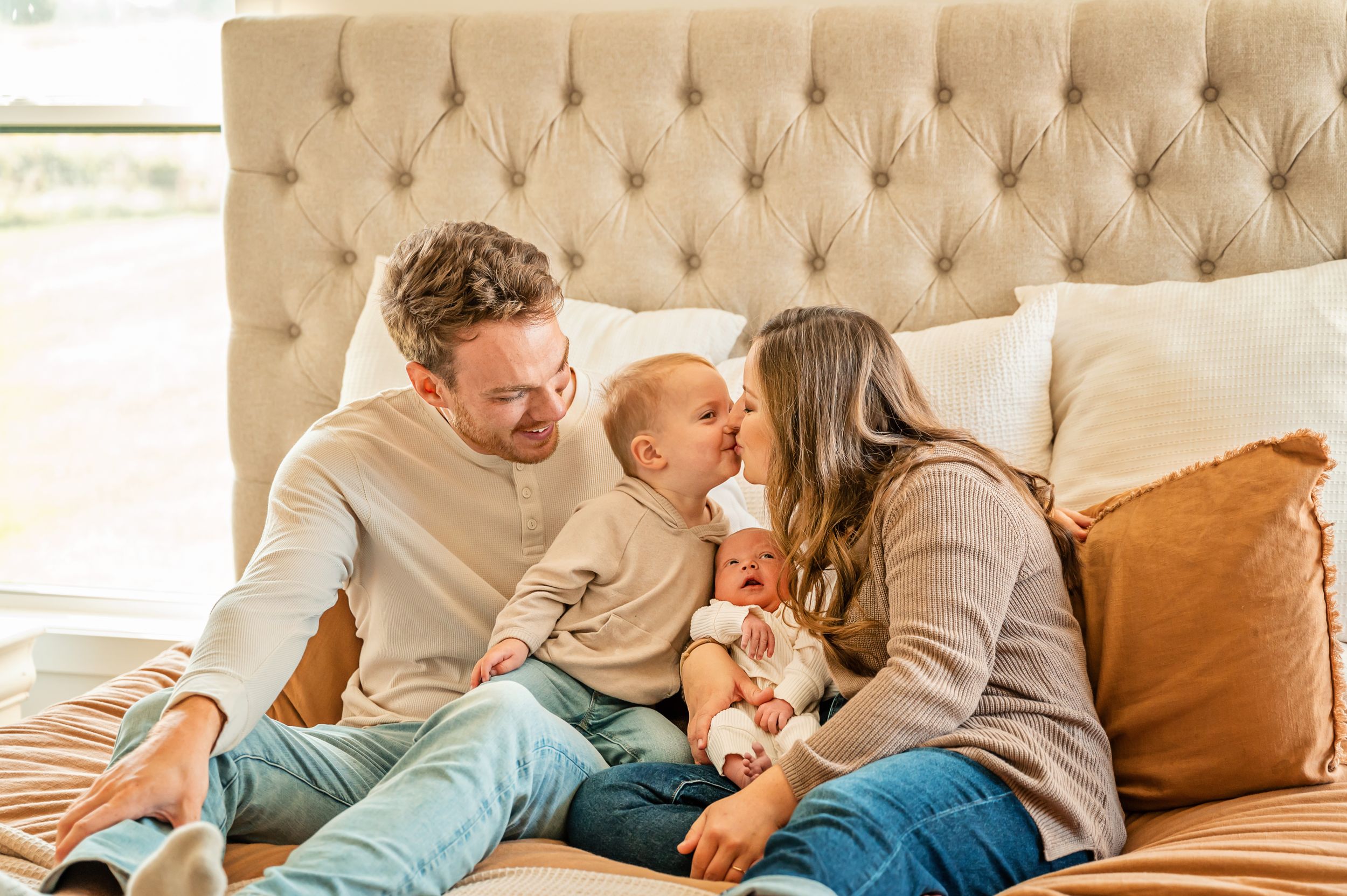 Family sharing an intimate moment together on beige tufted couch with orange accent pillows.