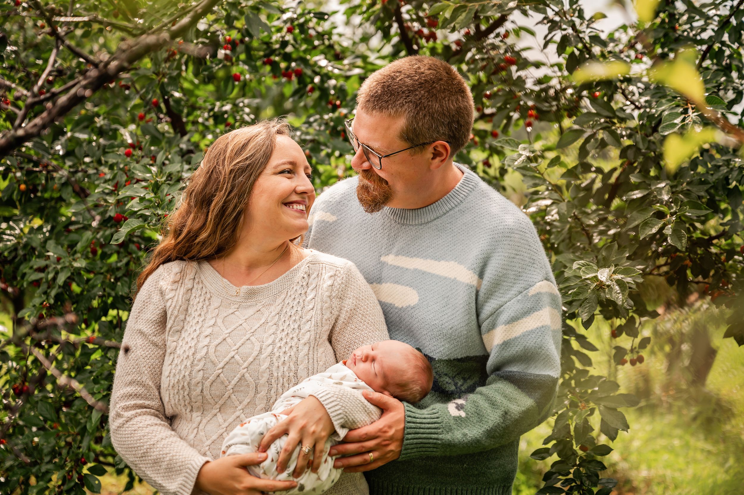 Family enjoying tender moments with their newborn baby outdoors in a lush garden setting.