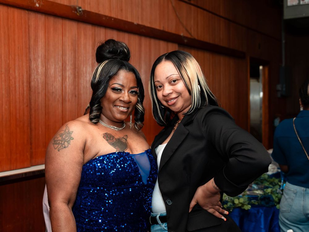Two friends pose together at an event, one wearing a sparkly blue dress and another in black.