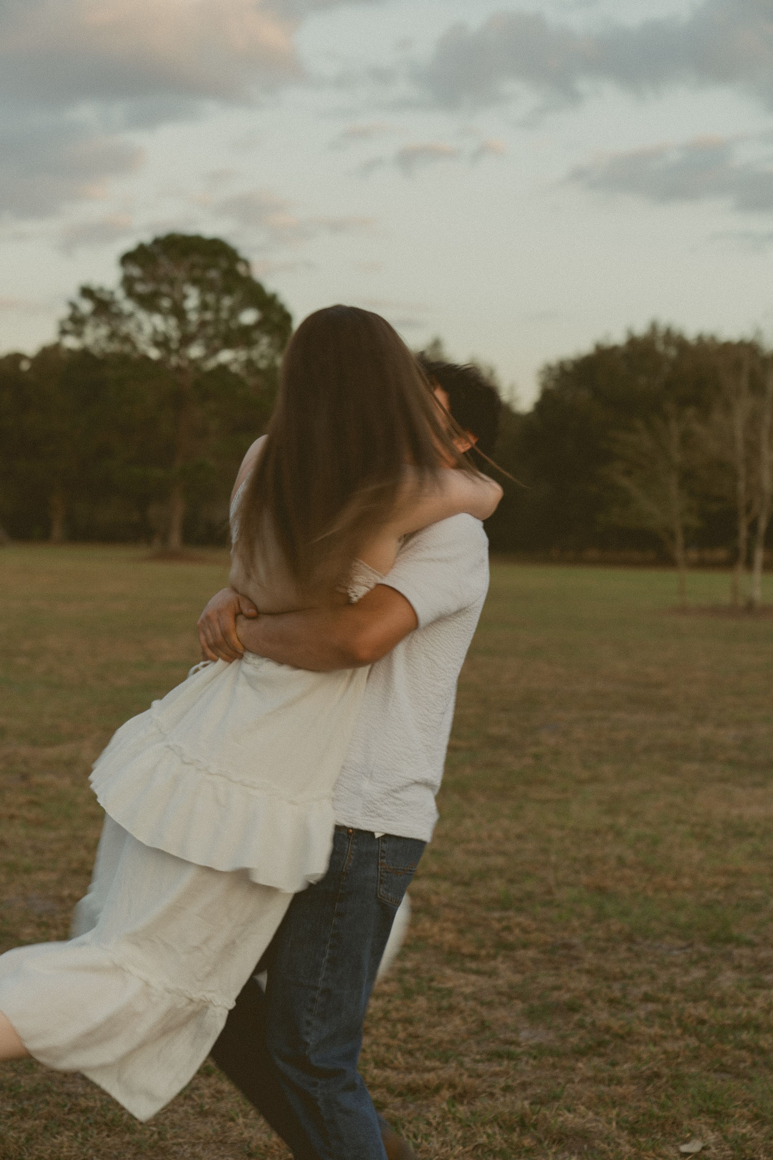 A couple in casual attire dancing together in a grassy field at sunset, captured in a series of romantic motion shots.