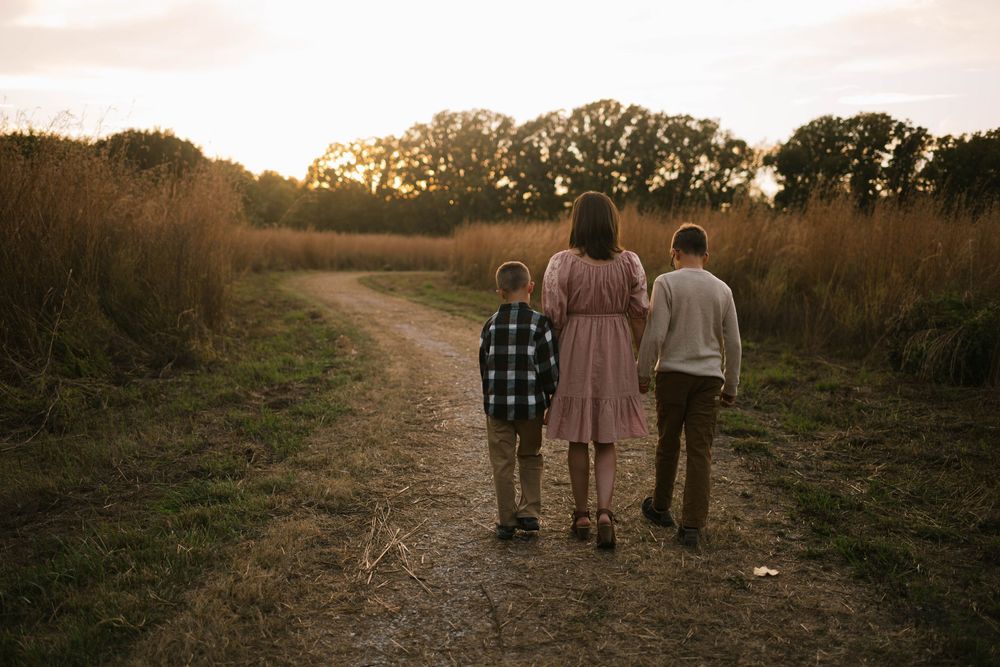 Candid photograph of a mother and her two young sons walking hand in hand through a natural outdoor setting