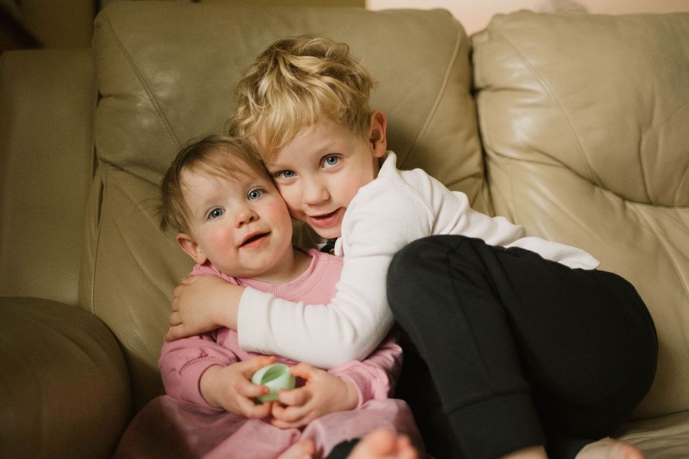 Candid shot of two siblings sharing a warm hug while sitting on a cozy couch, captured by Jess Volkman Photography in Centr
