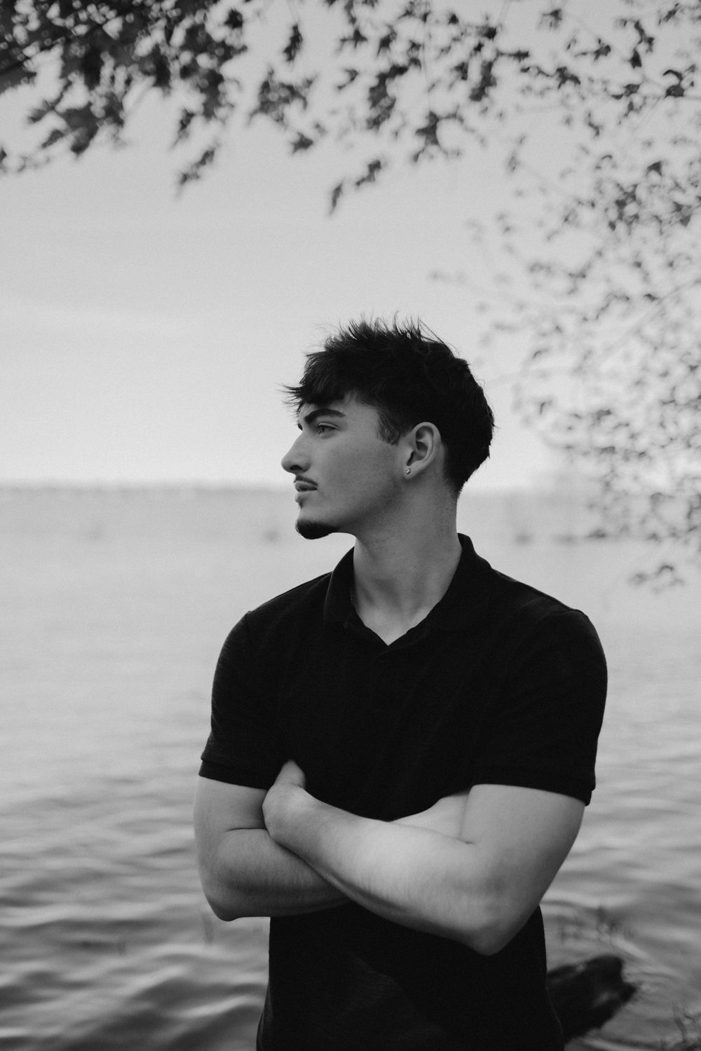 Black and white portrait of a senior boy posing by Lake Springfield, looking off into the distance.