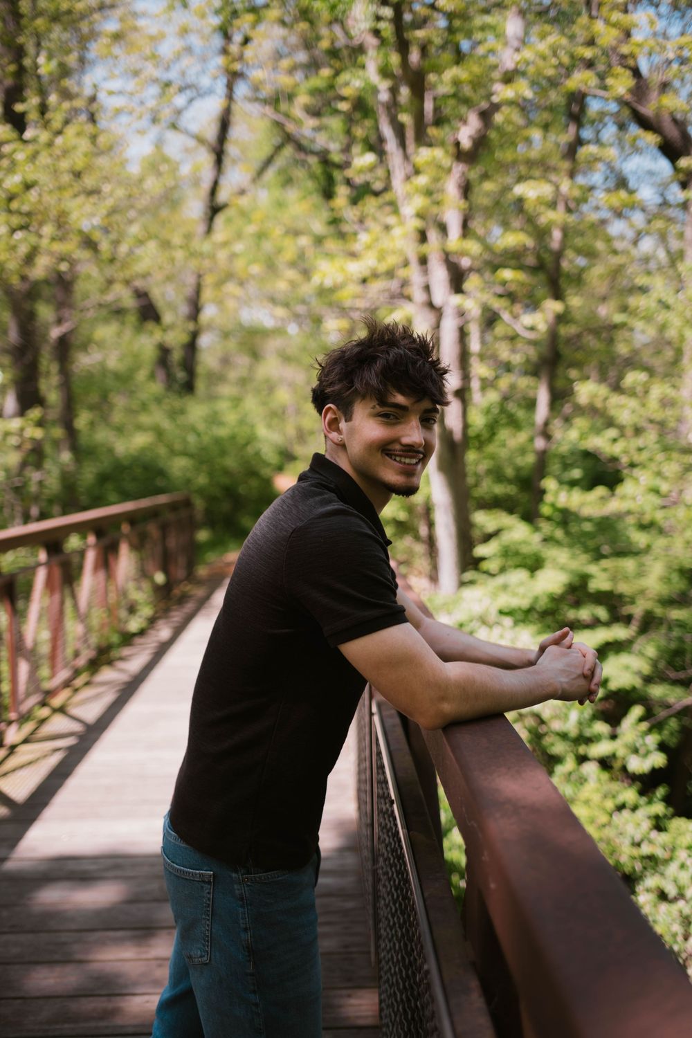 Senior boy posing on a rustic wooden bridge in a forest setting, captured by Jess Volkman Photography in Central Illinois.