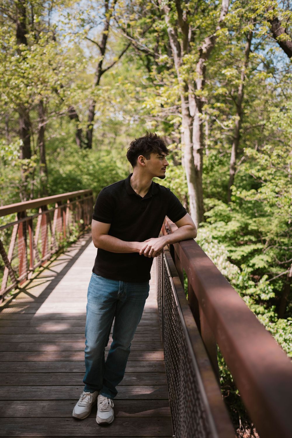 Senior boy posing on a rustic wooden bridge in a forest setting, captured by Jess Volkman Photography in Central Illinois.