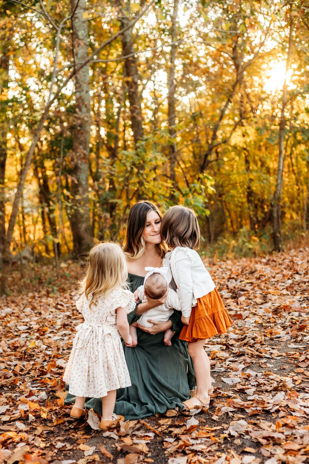 Family sits together on fallen autumn leaves during sunset photo session in wooded area in New Haven, CT.