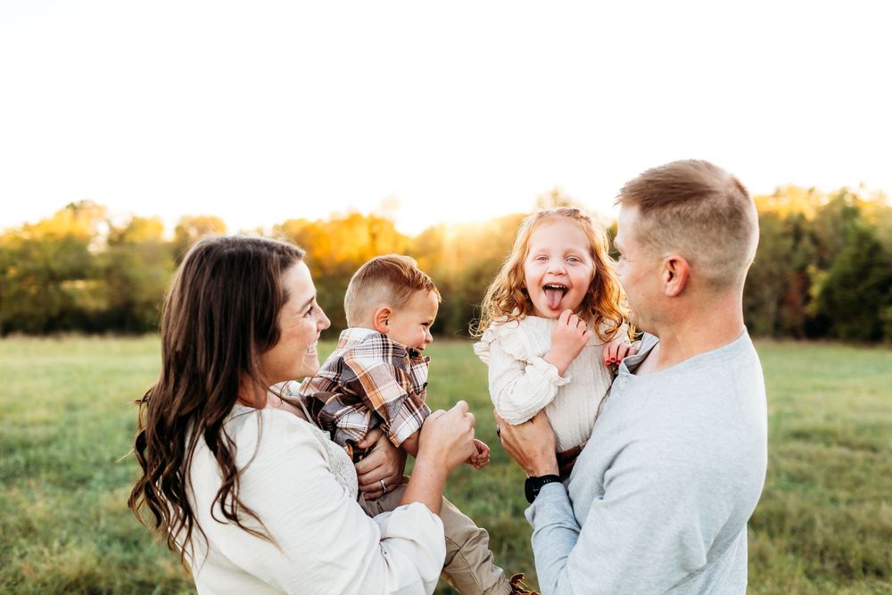 A mother and father kiss while holding their babies next to a forest  near Middlebury, CT during an Autumn session