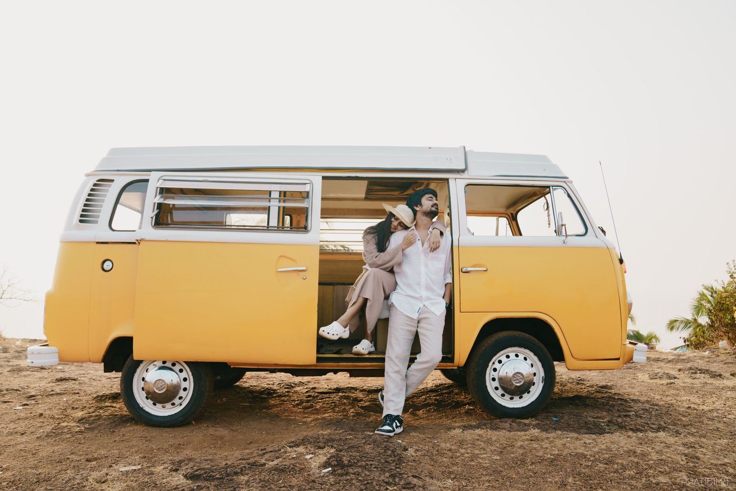 Couple sitting in a vintage yellow Volkswagen camper van on a rocky terrain during golden hour.