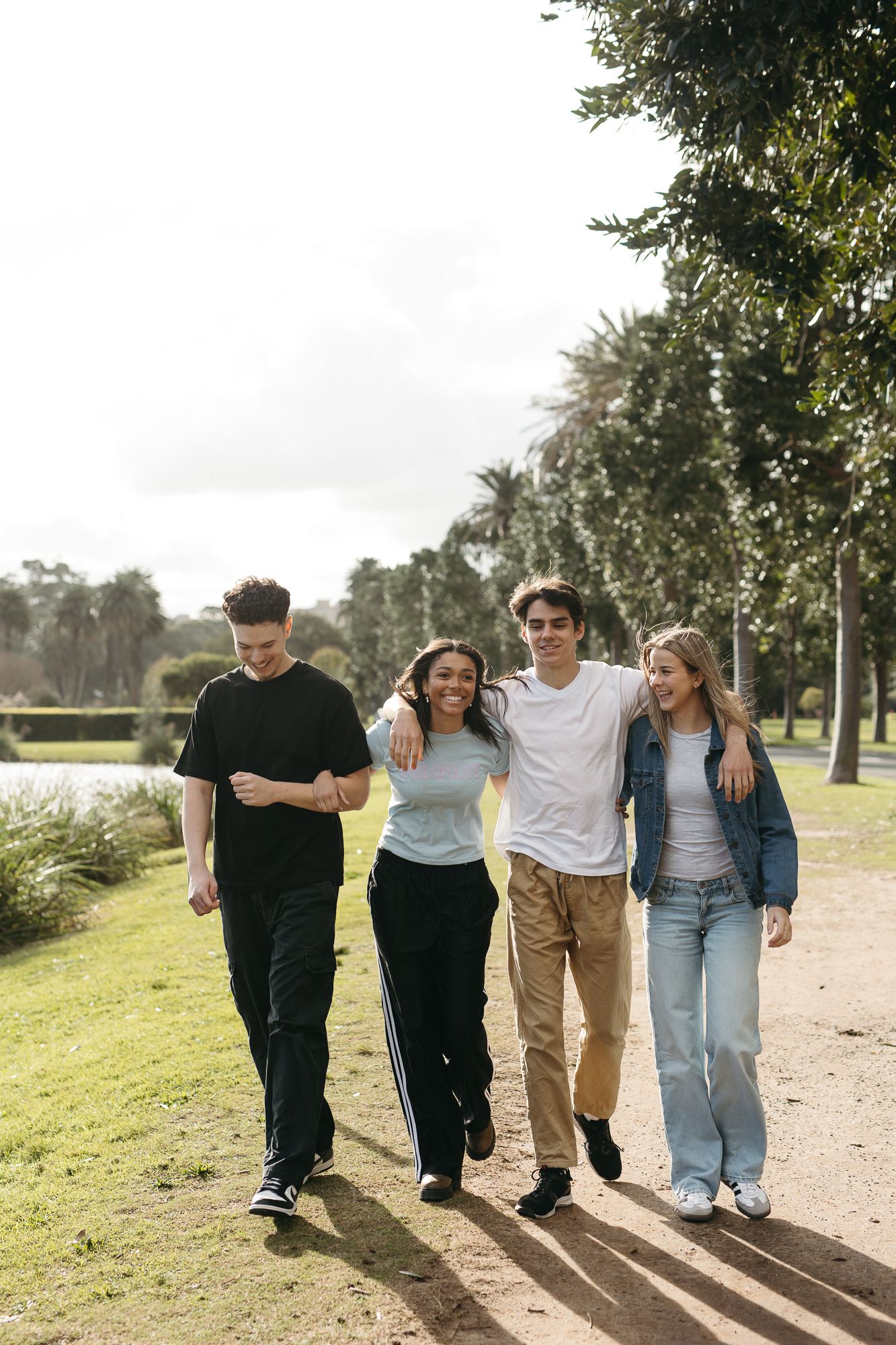 Four young friends walking together in a sunny park, smiling and enjoying each other's company outdoors.