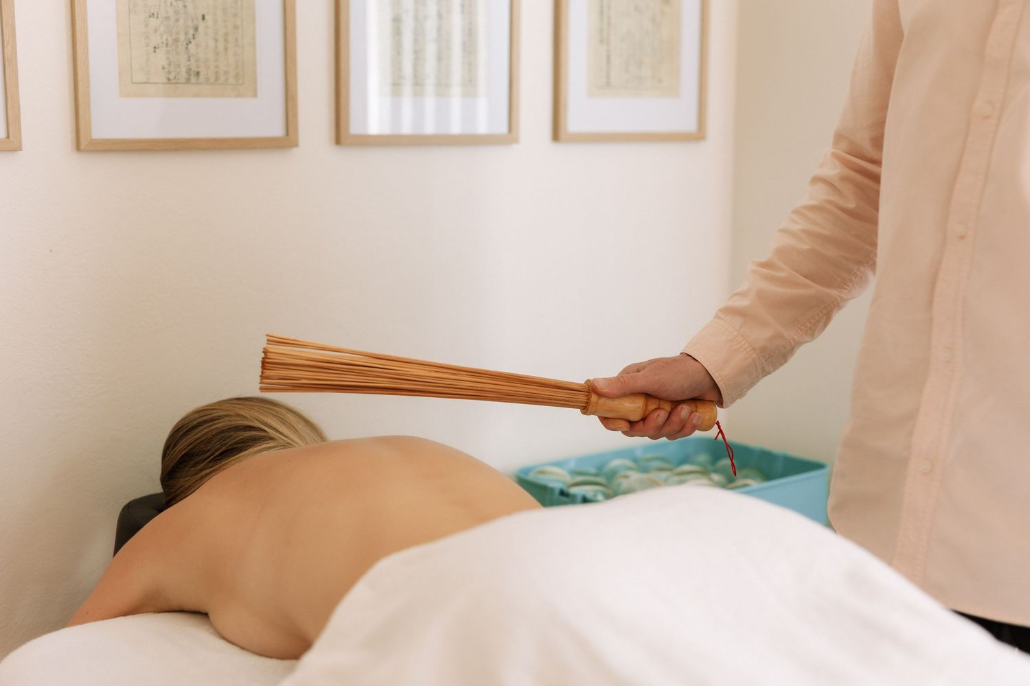 Therapist performing a bamboo massage treatment on a client lying face down on a massage table.