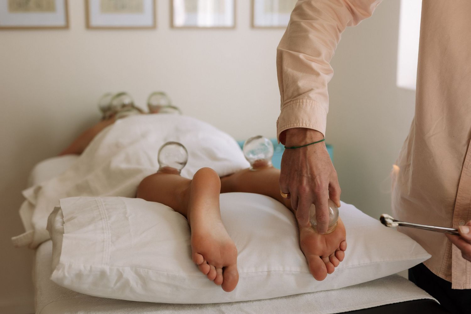 Therapist performing a foot massage on a client lying on a treatment table with white pillows.